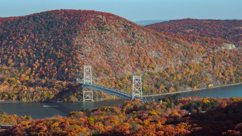 Bear Mountain Bridge Bear Mountain Bridge passes over the Hudson River. The trees along the rivers and mountains are in full autumn glory.