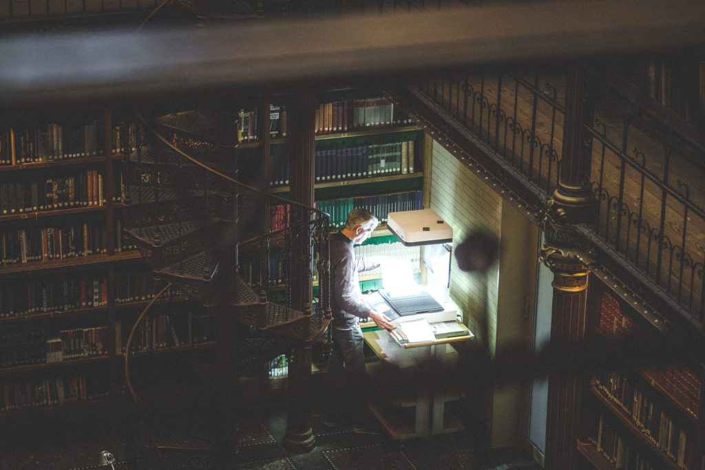 The Archivist A man, surrounded by the old books of a library, is illuminated by the glow of the document scanner he is using.