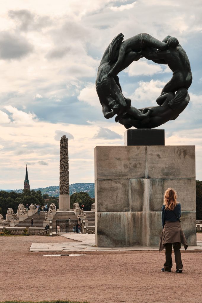 Viglandsparken A woman admiring a sculpture in a park,with more sculptures and a church visible in the background